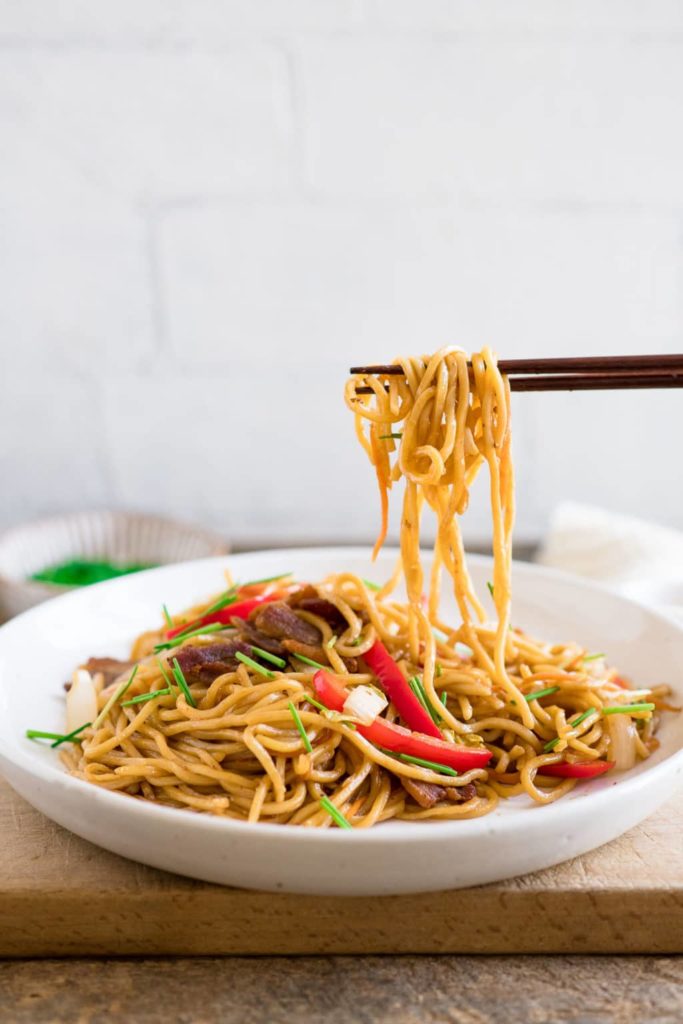 pair of chopsticks lifting strands of yakisoba noodles from a plate