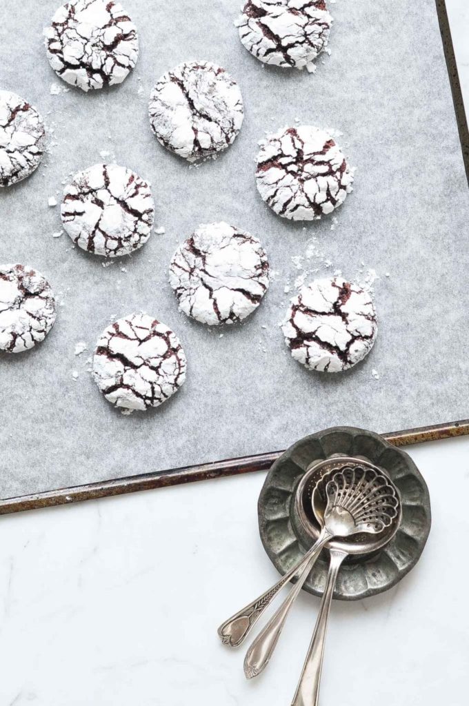 chocolate crinkle cookies on baking tray with metal spoons