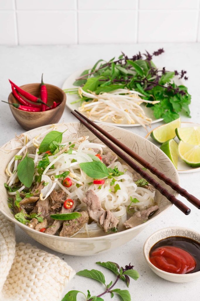bowl of vietnamese pho with slices of beef and fresh herbs