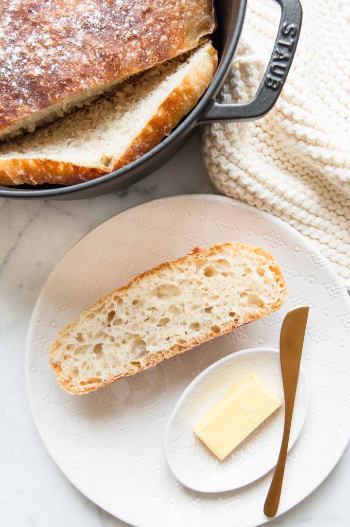 slice of no-knead bread on white plate with butter