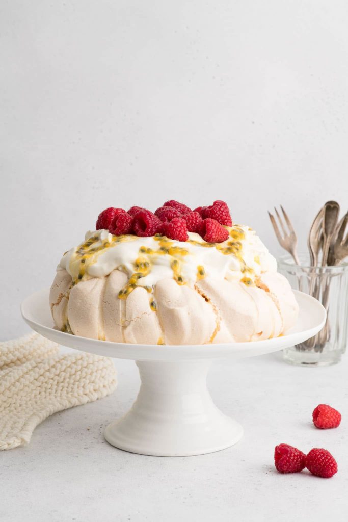 passionfruit with whipped cream, passionfruit and raspberries on cake stand with forks
