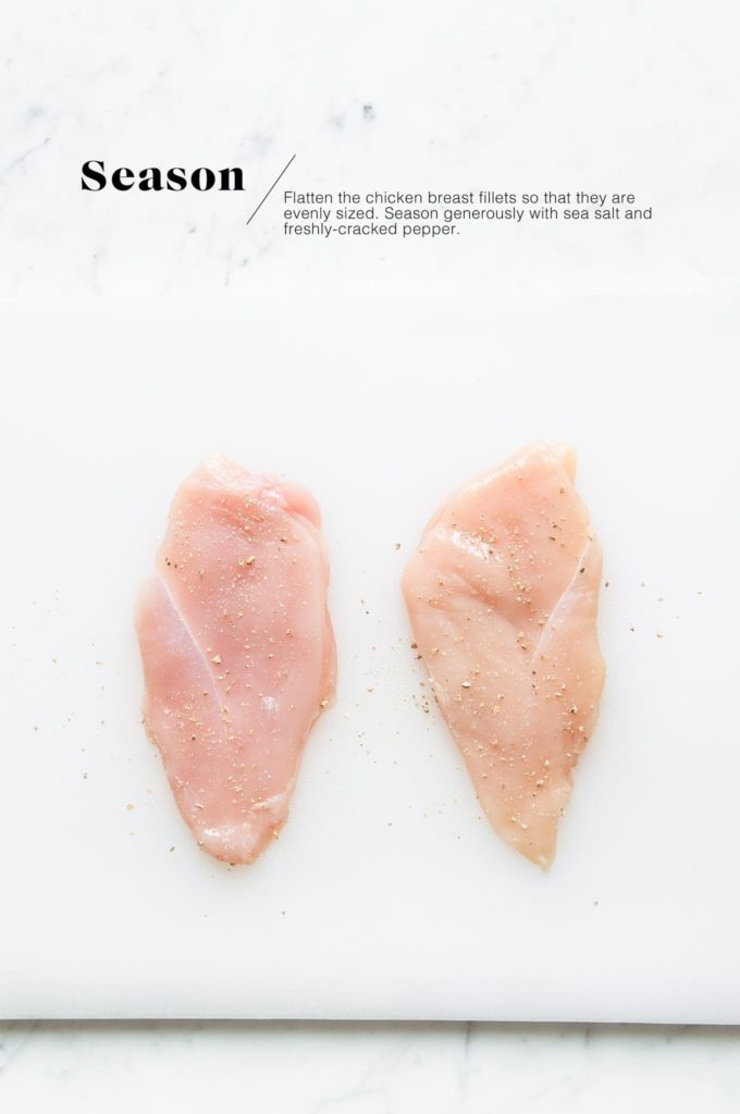 raw chicken breast fillets with salt and pepper on chopping board