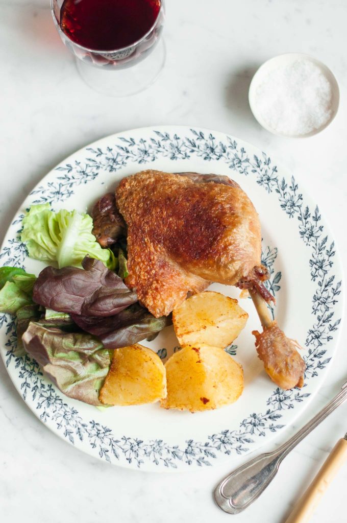 duck confit leg on plate with salad and potatoes
