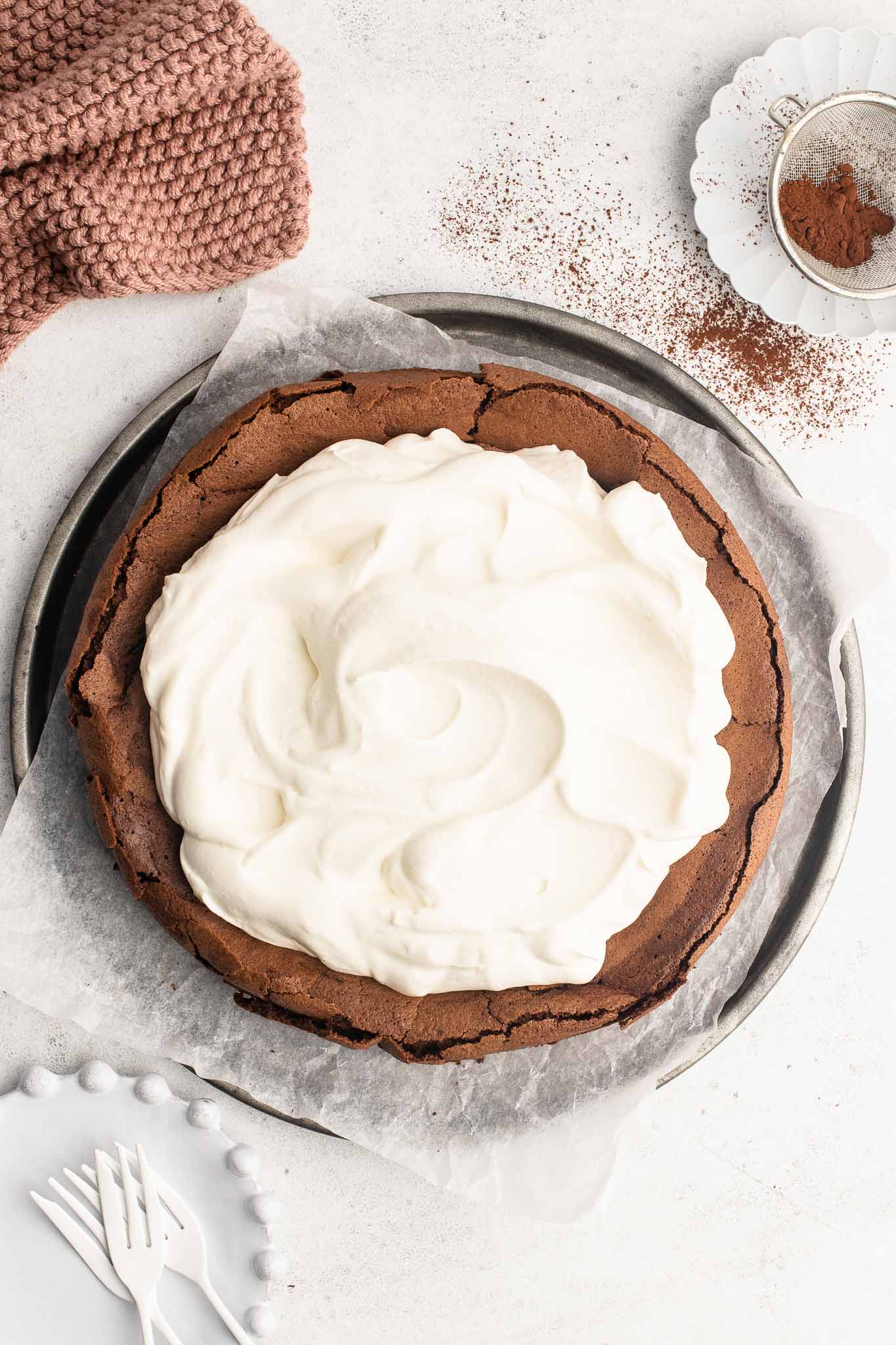 flourless chocolate cake with whipped cream on metal tray with pink cloth