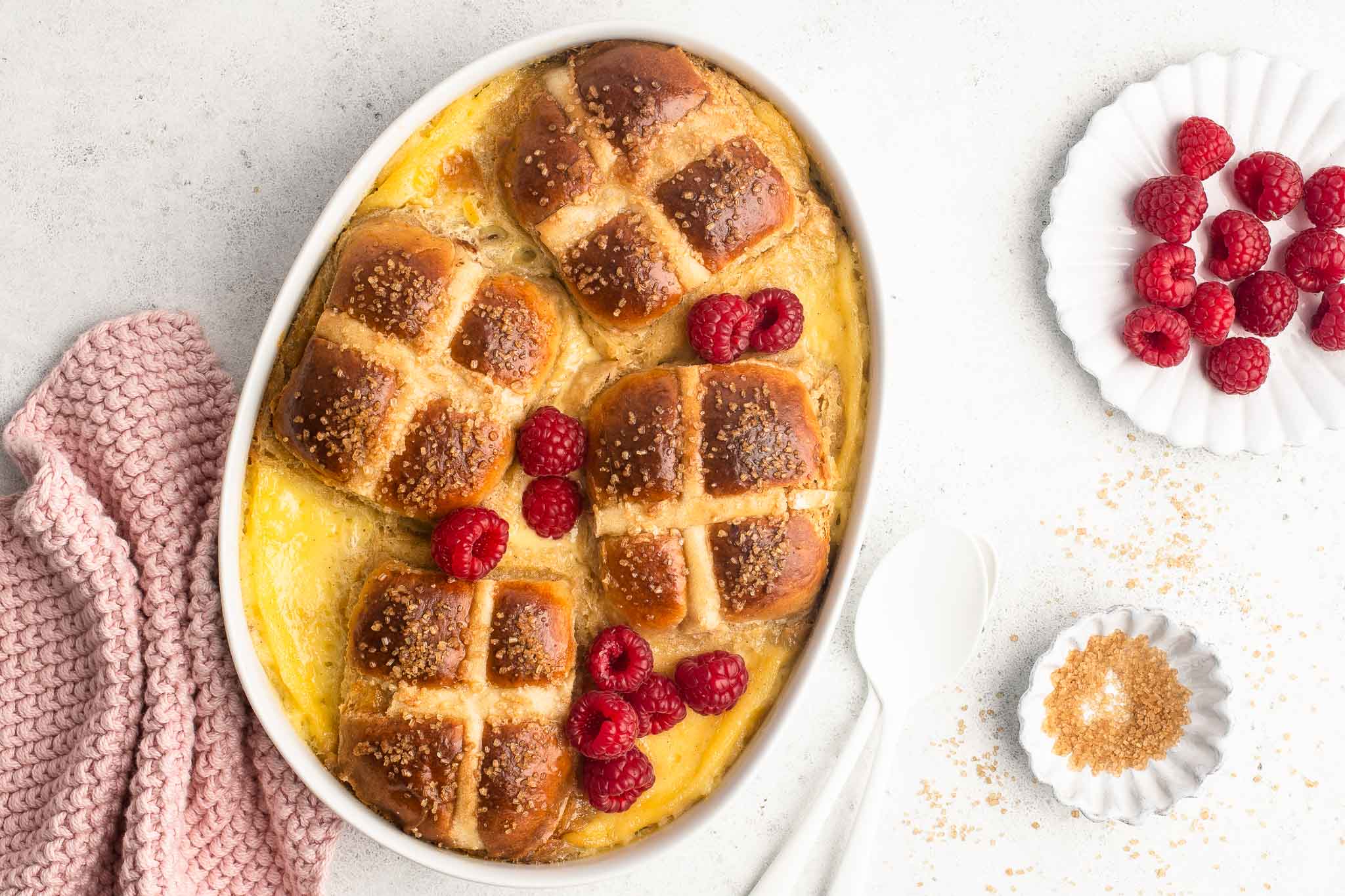 hot cross bun bread and butter pudding in white dish with raspberries