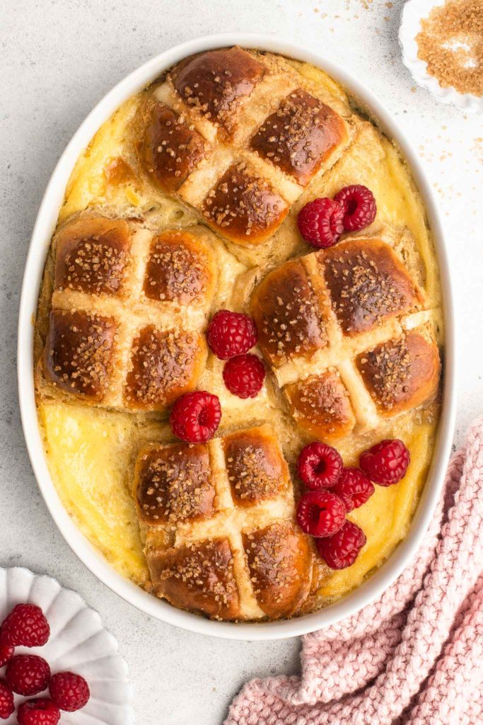 hot cross bun bread and butter pudding with fresh raspberries in oval baking dish