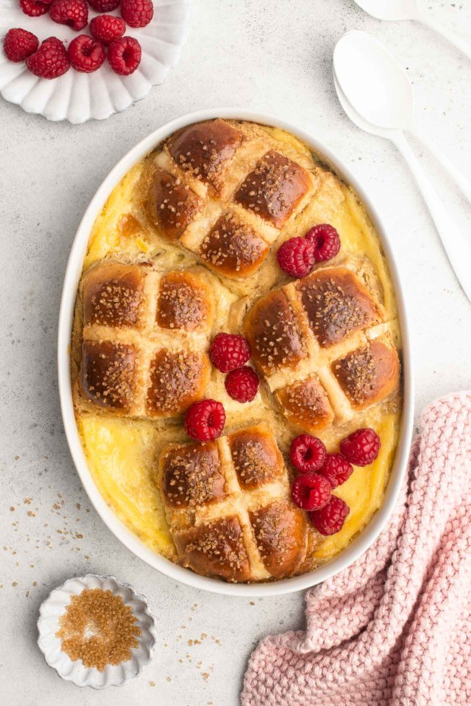hot cross bun bread and butter pudding with raspberries in white oval dish