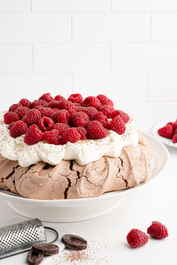 chocolate pavlova with whipped cream and raspberries on cake stand