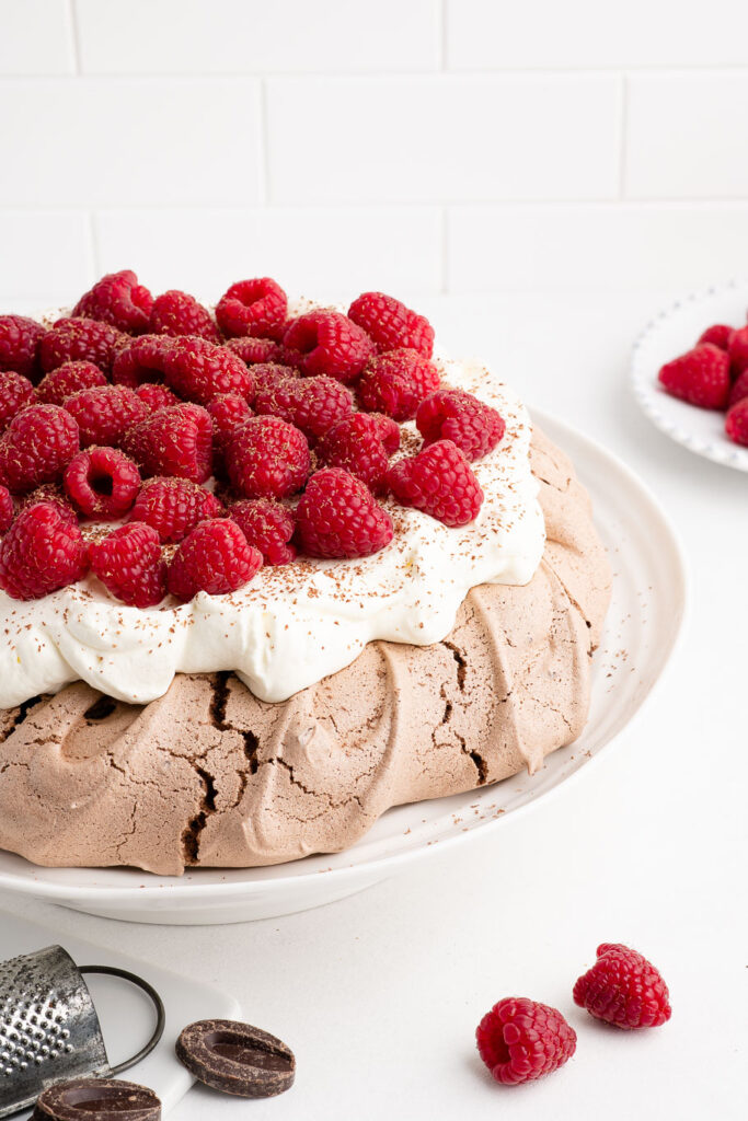 chocolate pavlova with whipped cream and fresh raspberries on white cake plate