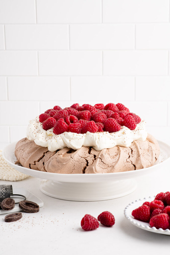 chocolate pavlova with whipped cream and fresh raspberries on white platter