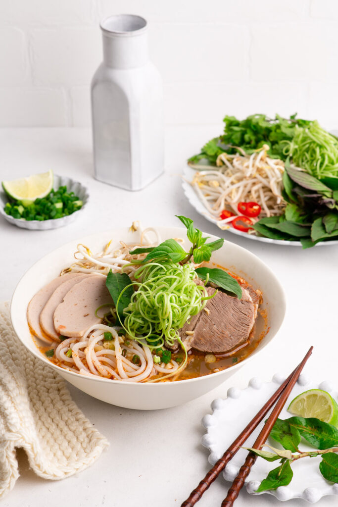 bun bo hue in noodle bowl with water spinach