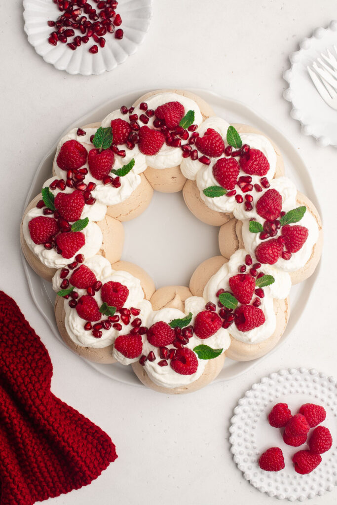 christmas pavlova wreath with fresh raspberries, pomegranate seeds and mint on white platter