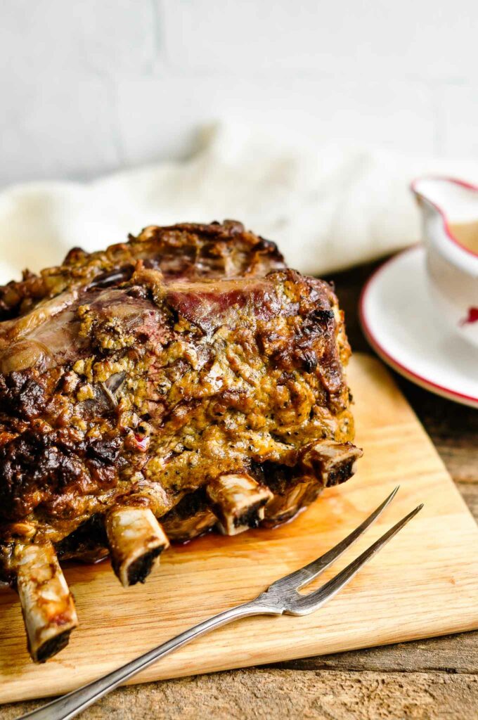 standing rib roast on wooden board with serving fork
