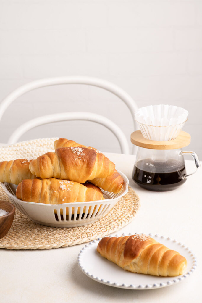 salted butter rolls in a basket with coffee pot
