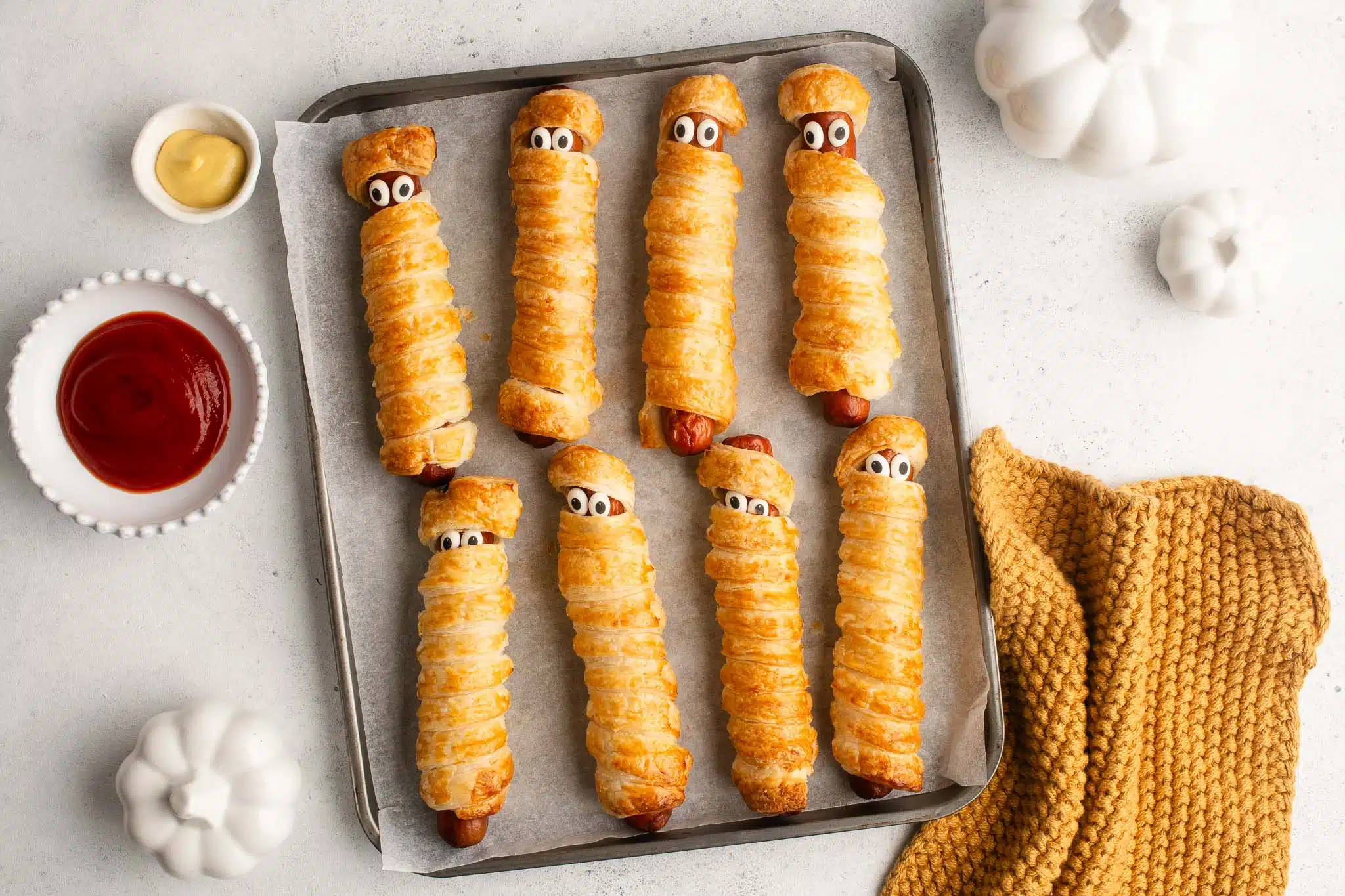hot dog mummies with ketchup and mustard on baking tray
