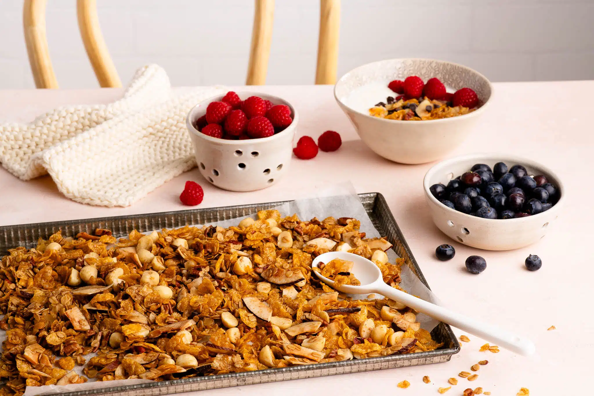 homemade granola on baking tray with bowls of fresh berries