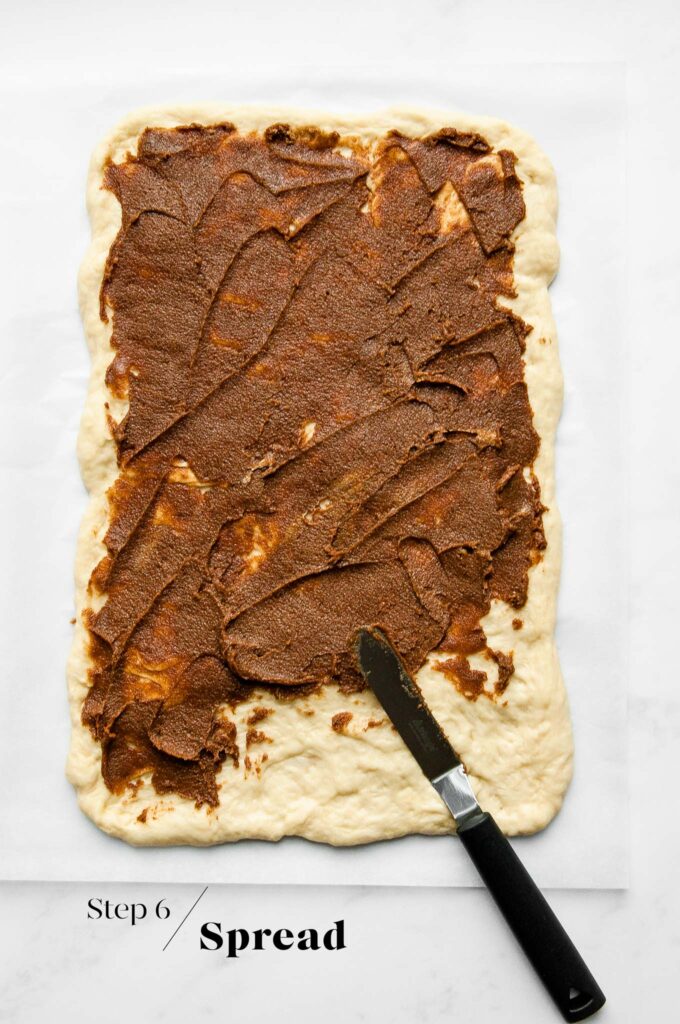 spreading cinnamon butter on dough with spatula