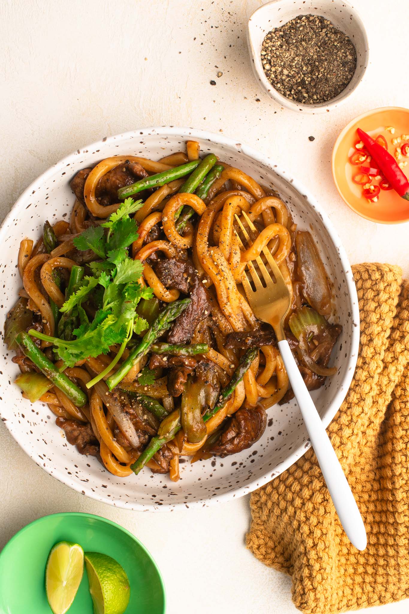black pepper beef noodles with coriander and asparagus in white speckled bowl